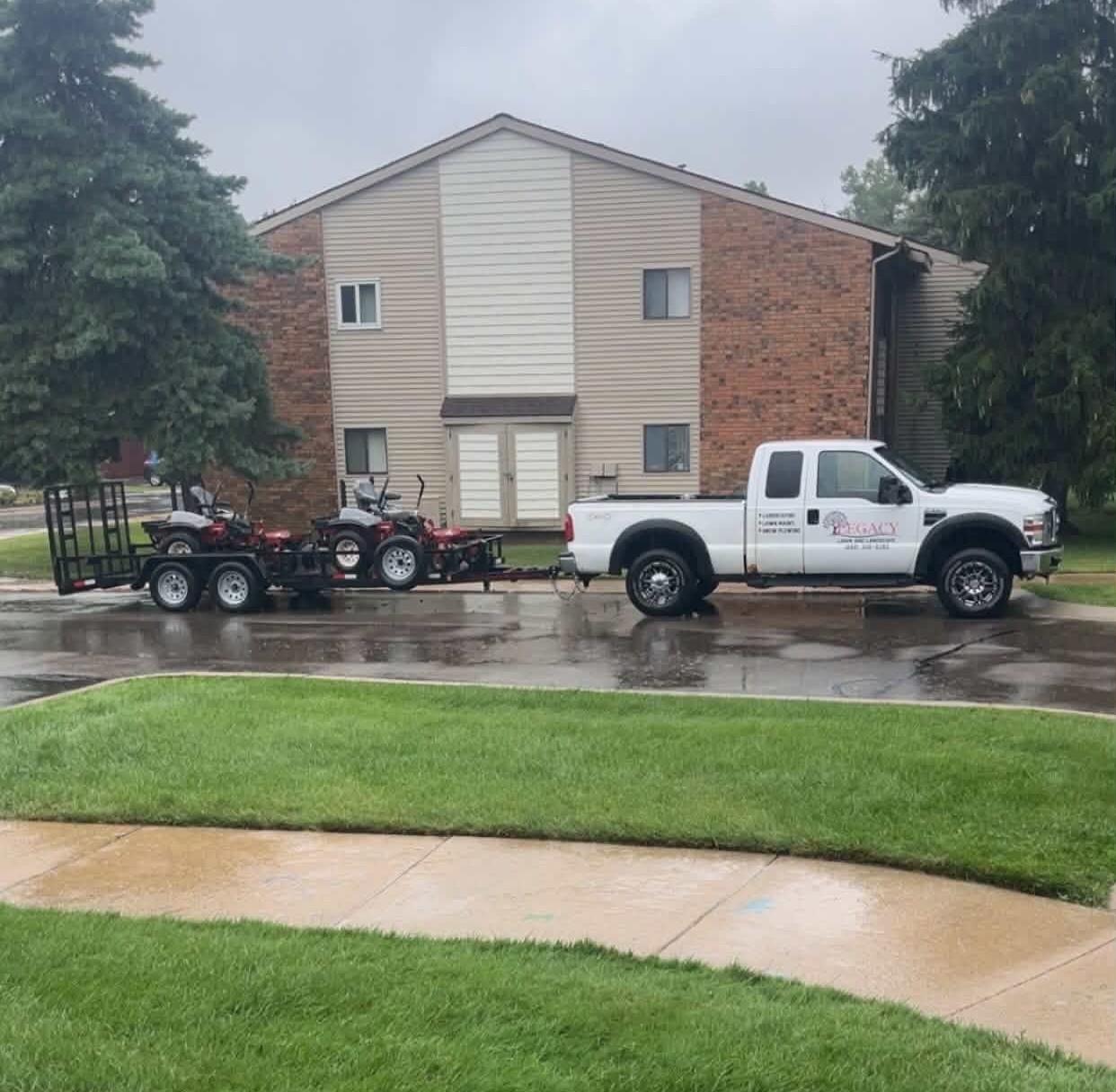 Legacy Lawn And Landscape work truck and trailer loaded with mowers on a job site